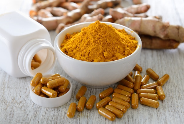 Capsule di curcuma e curcuma su superficie di legno