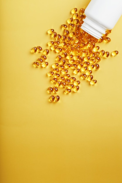 Capsule di olio di pesce Omega3 dorate versate da un barattolo su sfondo giallo