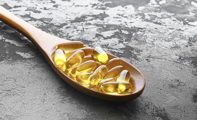 Capsule di omega-3 in cucchiaio di legno su uno sfondo di cemento sbiadito