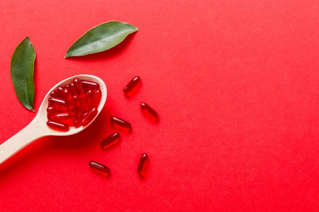 Capsule di vitamine in un cucchiaio su uno sfondo colorato Pillole servite come un pasto sano Capsule di integratori vitaminici in gel morbido rosso sul cucchiaio