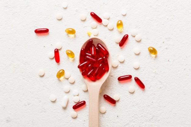 Capsule di vitamine in un cucchiaio su uno sfondo colorato Pillole servite come un pasto sano Capsule di integratori vitaminici in gel morbido rosso sul cucchiaio
