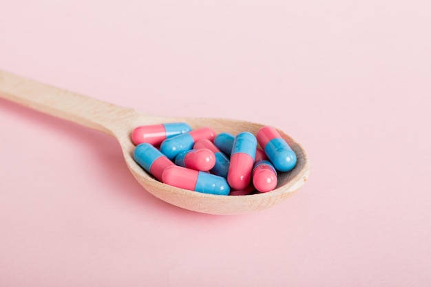 Capsule di vitamine in un cucchiaio su uno sfondo colorato Pillole servite come un pasto sano Capsule di integratori vitaminici in gel morbido rosso sul cucchiaio