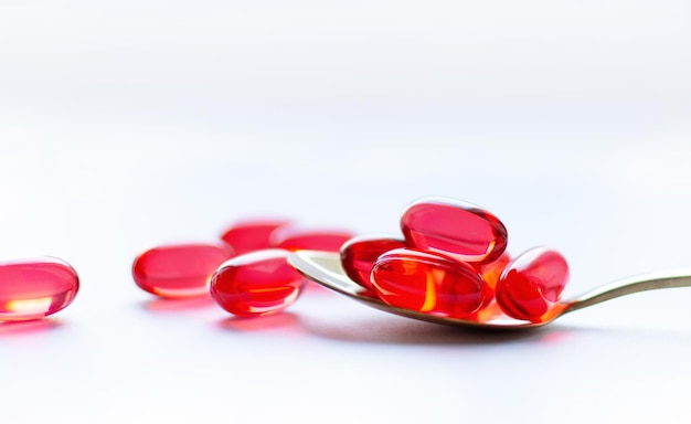 Capsule rosse in un cucchiaio d'oro su sfondo bianco Concetto di farmacia Trattamento di medicina tradizionale