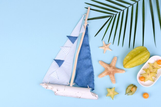 Carambola di frutta, accessori da spiaggia e fogliame di una pianta tropicale su carta colorata. Sfondo estivo con stelle marine e frutti