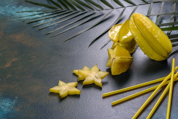 Carambola di frutta, accessori da spiaggia e fogliame di una pianta tropicale su carta colorata.