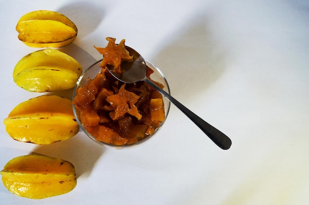 Carambola sciroppata all'interno di una ciotola con un cucchiaio con un pezzo all'interno e quattro frutti accanto alla ciotola