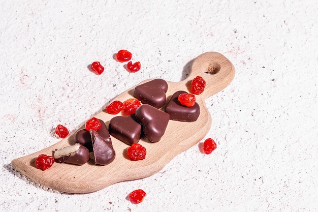 Caramelle al cioccolato a forma di cuore con ciliegie essiccate. Luce dura moderna, ombra scura. Un dolce regalo per San Valentino o un anniversario. Sfondo in gesso dai toni chiari, posto per il testo