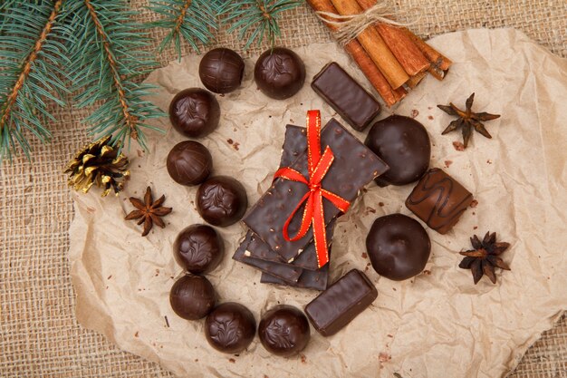 Caramelle al cioccolato di varie forme e barrette di cioccolato con noci messe su un pezzo di carta da pacco a forma di cuore con anice stellato, cannella e ramo di abete. Vista dall'alto