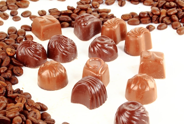 Caramelle al cioccolato e chicchi di caffè isolati su bianco