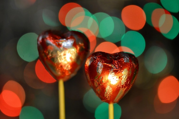 Caramelle al cioccolato per San Valentino Cioccolato a forma di cuore rosso su bastoncino per lecca-lecca Cuore di cioccolato in lamina rossa su un bastoncino su sfondo bokeh sfocato