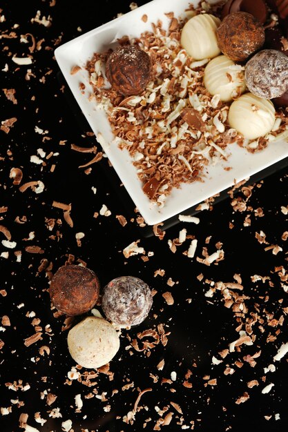 Caramelle di cioccolato assortite su piatto bianco con scaglie su sfondo nero