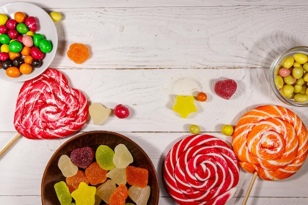 Caramelle di cioccolato colorate, lecca-lecca e caramelle gelatinose su un tavolo di legno bianco