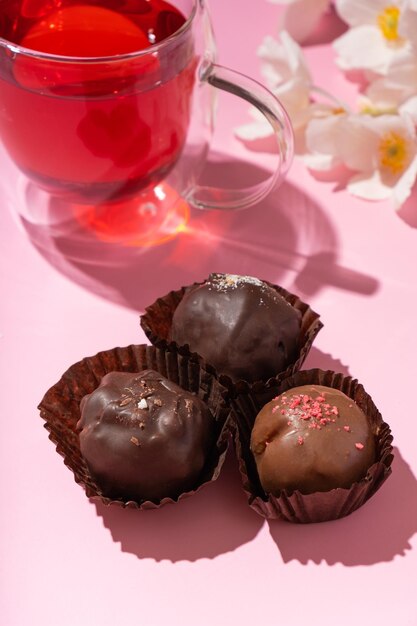 Caramelle di noci artigianali al cioccolato su sfondo rosa con tazza di tè e fiori Dolci per bere il tè