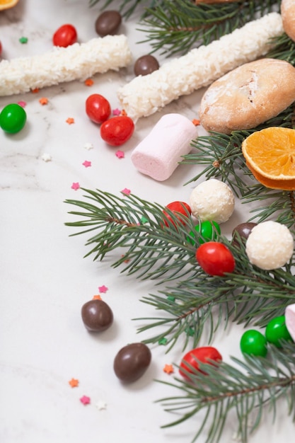 Caramelle e biscotti con rami di albero di Natale su sfondo di marmo bianco