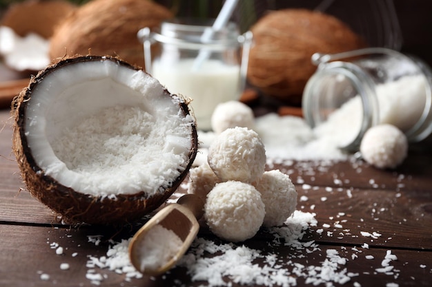 Caramelle in scaglie di cocco, bicchiere di latte e cocco fresco su fondo di legno scuro