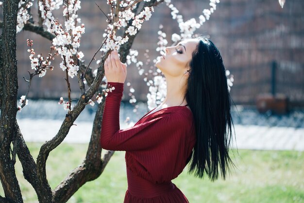 Caratteristica stagionale bellezza e moda bella donna vicino all'albero in fiore di albicocca