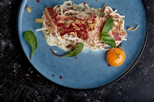 Carbonara di pasta classica con tuorlo su un piatto. Pasta presentata su un piatto blu su un buio. Concetto di cucina italiana, splendidi piatti da portata, primo piano.