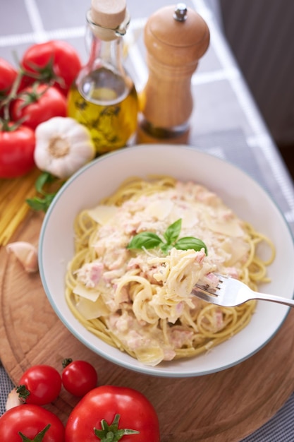 Carbonara di pasta fatta in casa con basilico fresco e parmigiano in piatto di ceramica