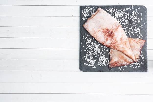 Carcassa di calamaro crudo con spezie e sale grosso su una tavola di ardesia nera. copia spazio Vista dall'alto.