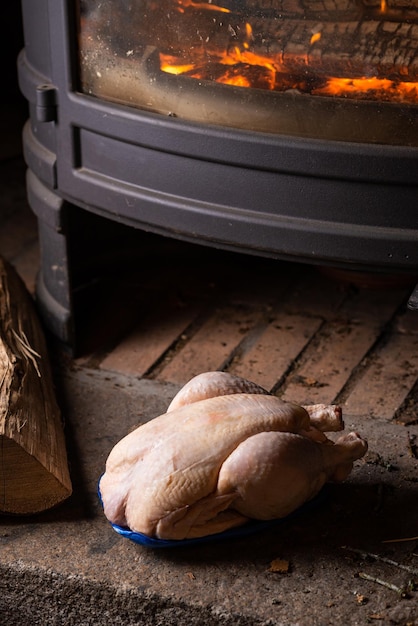 Carcassa di pollo crudo vicino al camino ardente