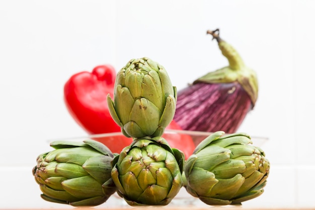 Carciofi verdi in primo piano e verdure rosse sullo sfondo