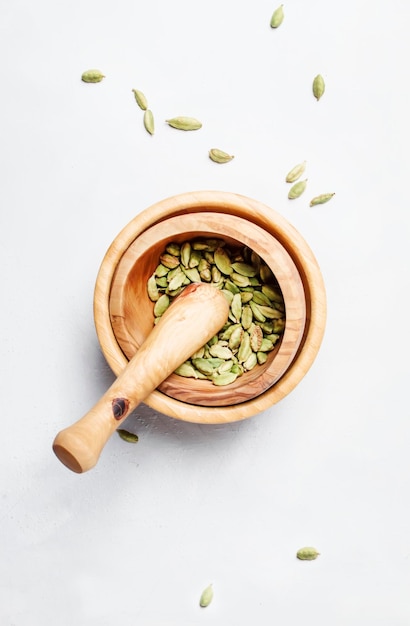 Cardamomo essiccato in ciotola di legno con vista dall'alto del fondo bianco del pestello