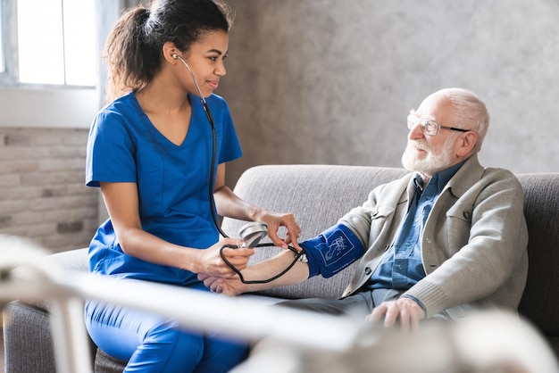 Cardiologa donna o medico che controlla l'alta pressione sanguigna che esamina un paziente maschio anziano utilizzando un tonometro durante la visita medica a casa i problemi cardiovascolari dell'ipertensione degli anziani concetto