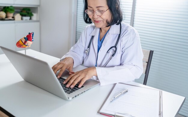 Cardiologo sostiene il cuore donna asiatica anziana medico che indossa occhiali e uniforme ritratto di matura vecchia donna asiatica medico professionista