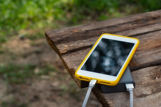 Caricabatterie portatile da viaggio. Power Bank carica uno smartphone su un tavolo di legno, sullo sfondo della natura. Concetto sul tema del turismo.