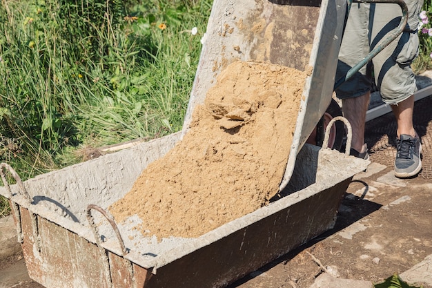 Caricamento della sabbia in una miscela di cemento per versare un percorso del giardino, lavori di costruzione su un orto