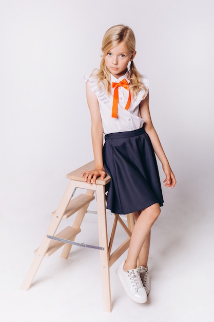 Carina adorabile ragazza bionda caucasica in uniforme scolastica su sfondo bianco