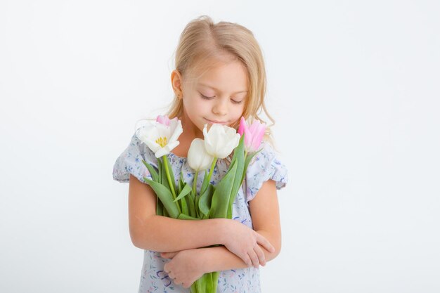 Carina bambina bionda in possesso di un mazzo di fiori primaverili su sfondo bianco