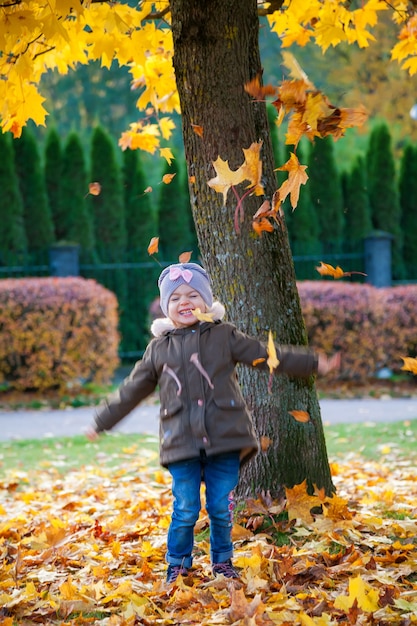Carina bambina di 3-4 anni felice che gioca nel parco autunnale. Caduta delle foglie d'autunno.
