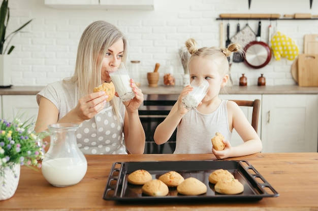 Carina bambina e mamma che mangiano biscotti appena sfornati con latte in cucina. Famiglia felice. Tonificante.