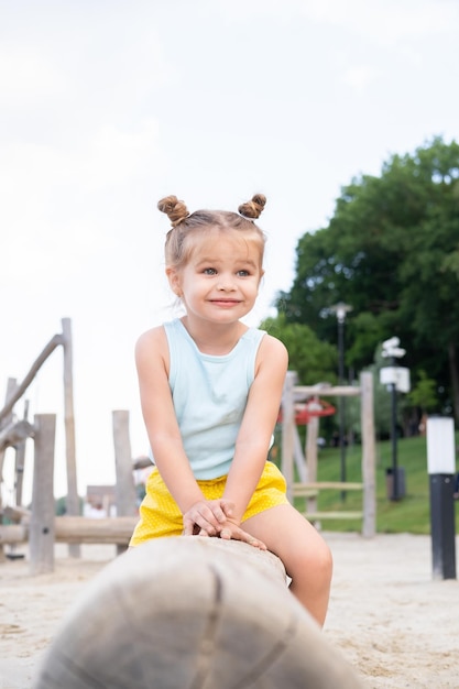 carina bambina in abiti colorati che giocano nel parco giochi per bambini in una giornata estiva