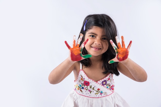 Carina bambina indiana che mostra le sue mani colorate o la stampa del palmo o gioca al festival di holi con i colori, isolato su sfondo bianco