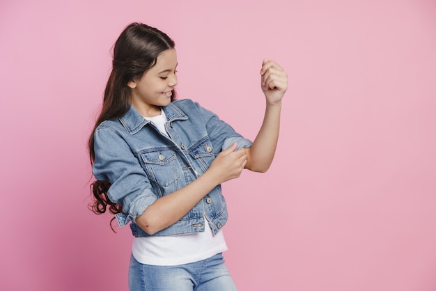 Carina, bella ragazza adolescente rimbocca le maniche di una giacca di jeans. Ragazza su sfondo rosa