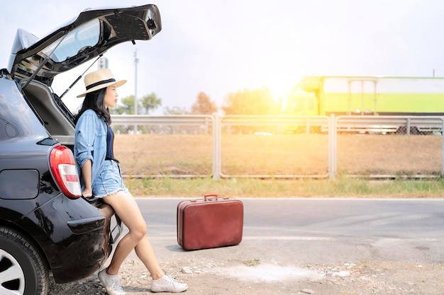 Carina donna asiatica seduta nel retro della sua auto completa di una borsa vintage rossa Auto parcheggiate sulla spalla della superstrada