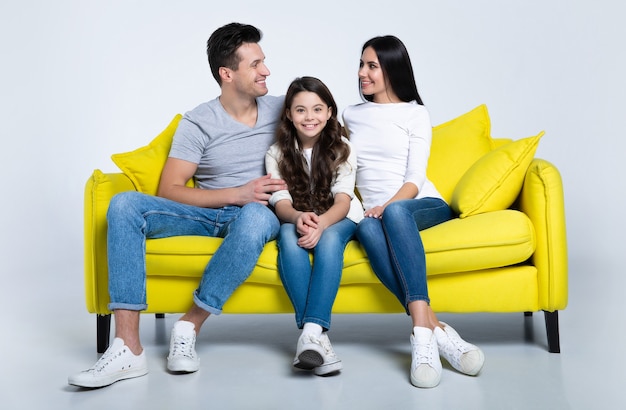 Carina famiglia di tre persone sedute sul divano giallo e sorridenti, godendosi il loro tempo insieme.