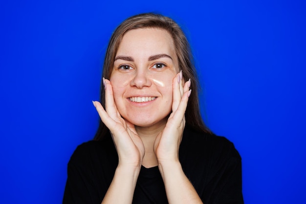 Carina giovane donna bionda con pelle liscia naturale senza trucco in posa felice e sorridente alla macchina fotografica mentre si trovava in maglietta su sfondo blu Concetto di bellezza bende per gli occhi per le donne