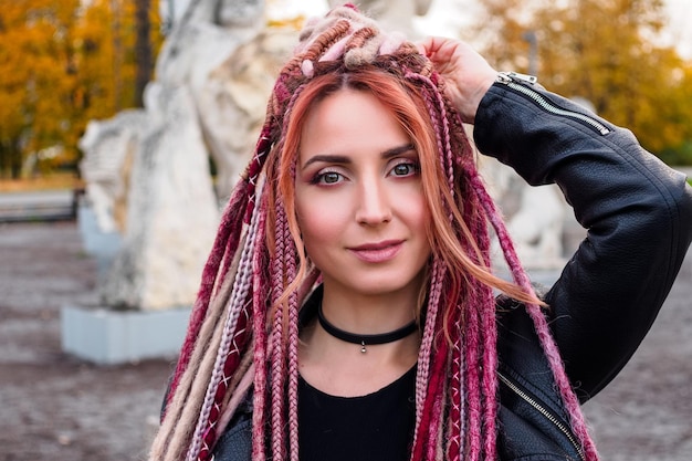 Carina giovane donna con i dreadlocks rosa e beige e le trecce guardando la telecamera e sorridendo