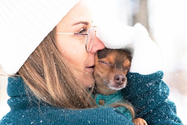 Carina, giovane donna in inverno bacia il suo cane, al freddo. Ragazza nella neve con un animale domestico di Chihuahua, si è bloccata.