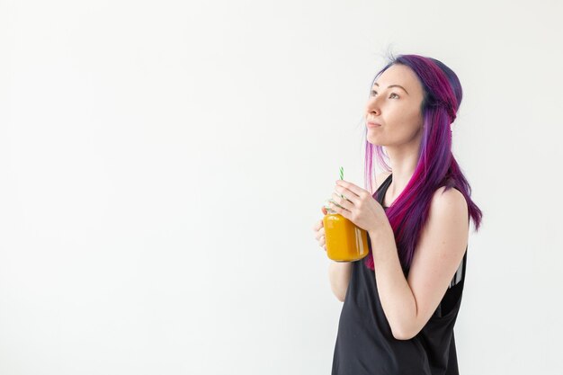 Carina giovane ragazza hipster di razza mista con capelli colorati beve frullato di frutta prima di iniziare uno yoga