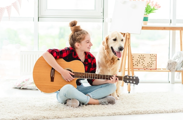 Carina ragazza adolescente a suonare la chitarra con bel cane al chiuso