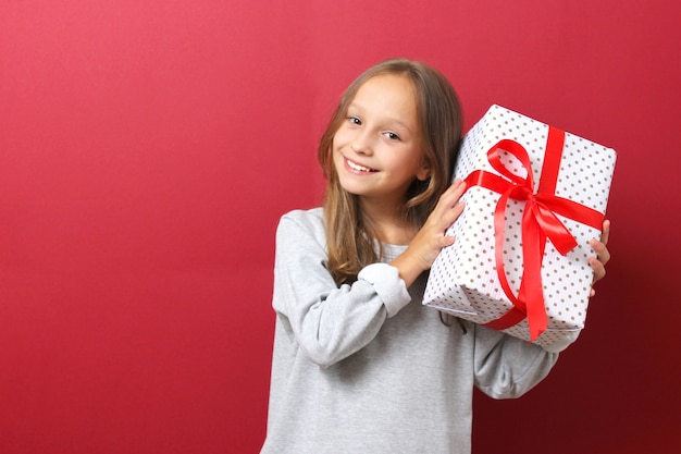 Carina ragazza allegra con un cappello di natale su uno sfondo colorato con in mano un regalo