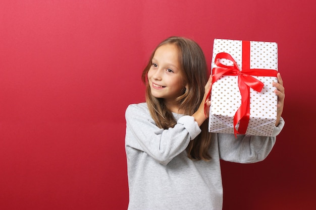 Carina ragazza allegra con un cappello di natale su uno sfondo colorato con in mano un regalo