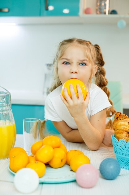 Carina ragazza allegra e divertente che tiene felicemente arance arancioni, con la cucina sullo sfondo