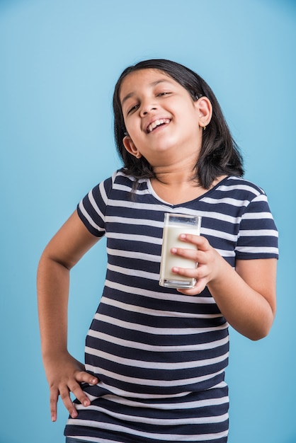Carina ragazza allegra indiana o asiatica che tiene o beve un bicchiere pieno di latte, isolato su uno sfondo colorato