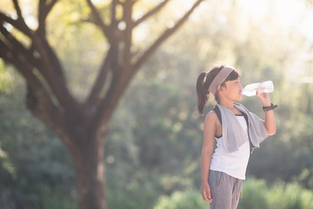 Carina ragazza asiatica beve acqua da una bottiglia all'aperto con la luce del sole