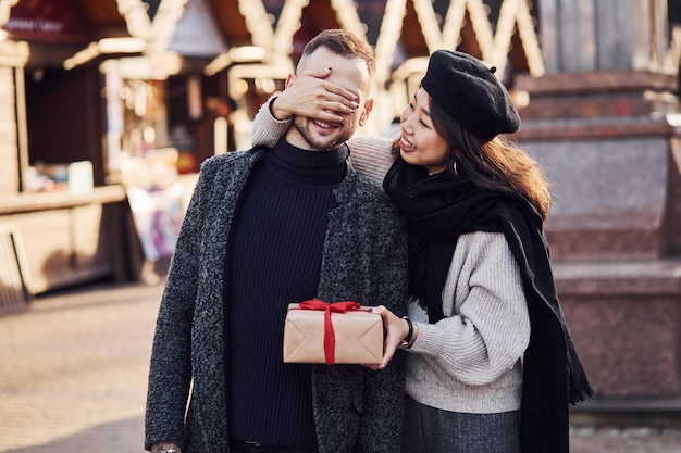 Carina ragazza asiatica che fa una sorpresa e regala una confezione regalo al suo uomo caucasico.